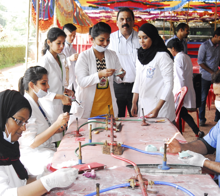 A group of dental students working with Bunsen burners at a table overseen by an International College of Dentists Fellow